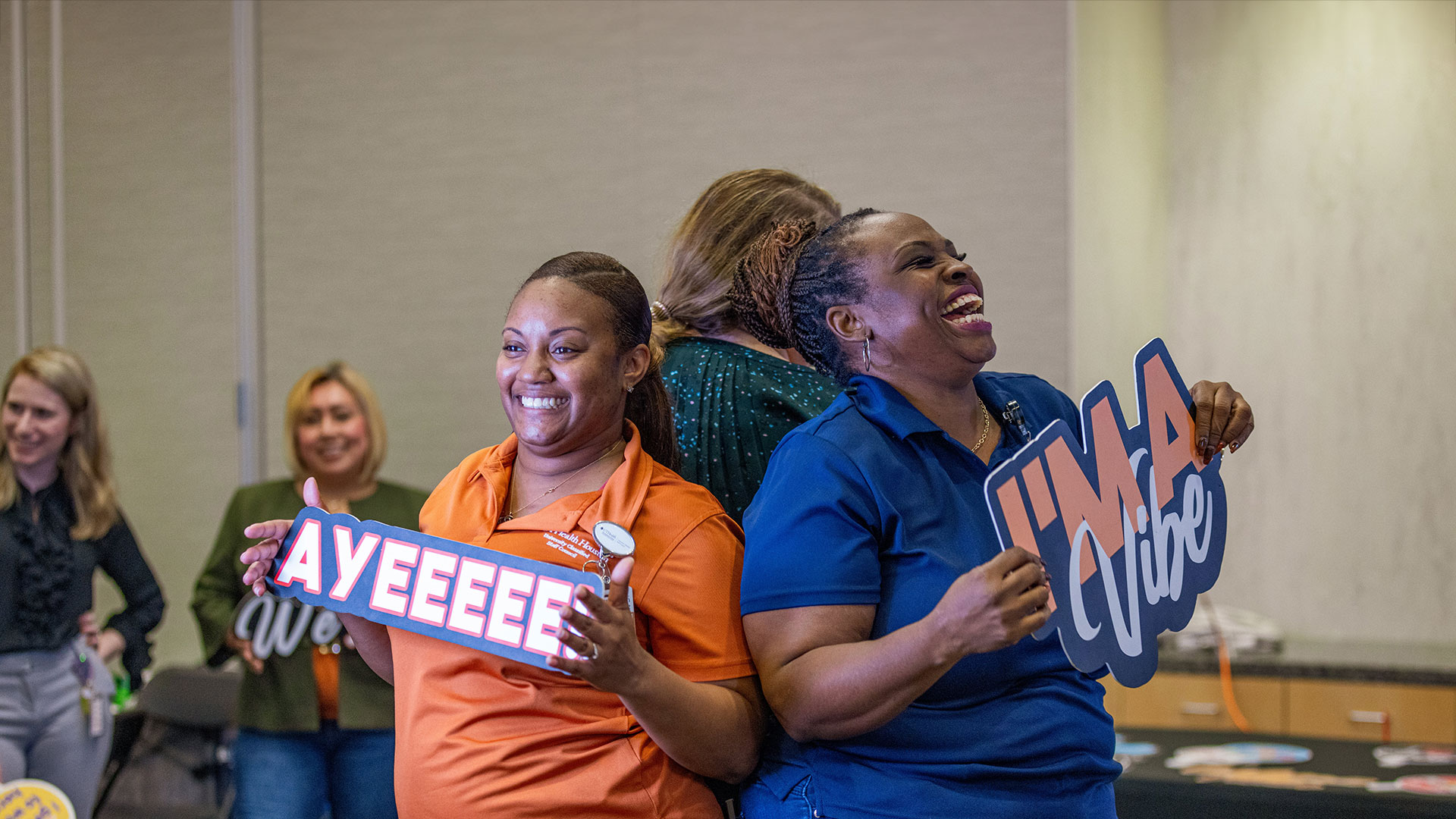 Two staff members of UTHealth Houston smiling and holding up signs that say I'm a vibe and ayyyyeeeeeeee